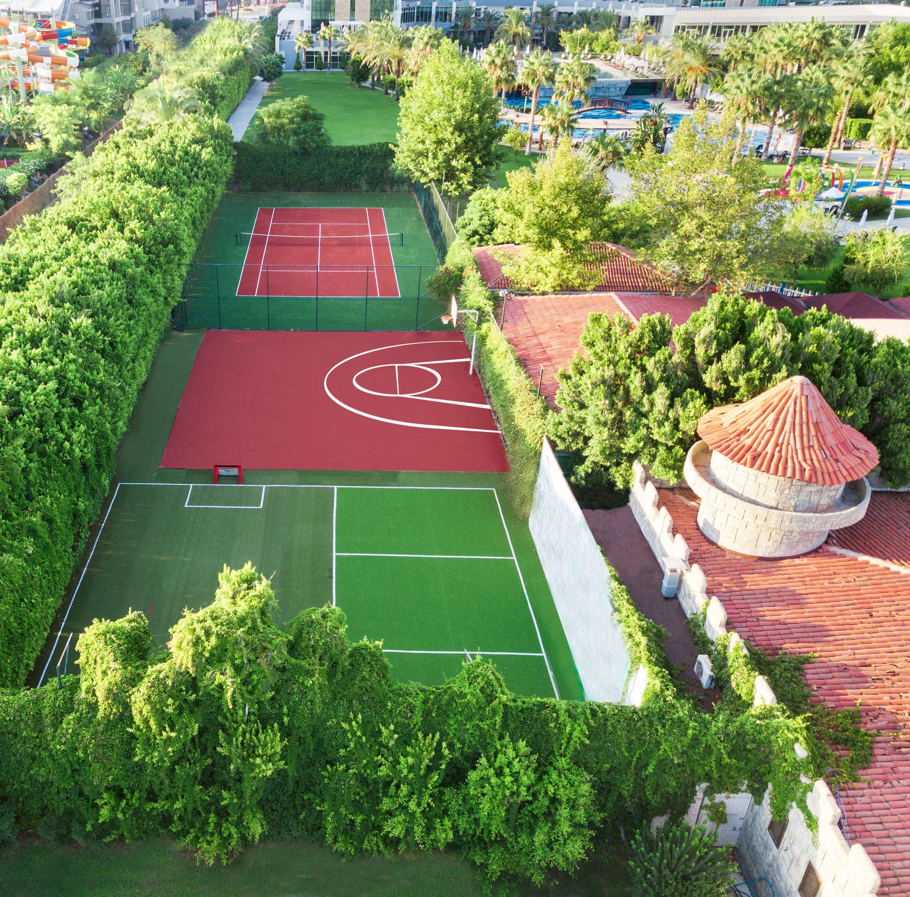 Luchtbeeld van een sportcomplex met meerdere tennisbanen, een zwembad en omliggend groen.