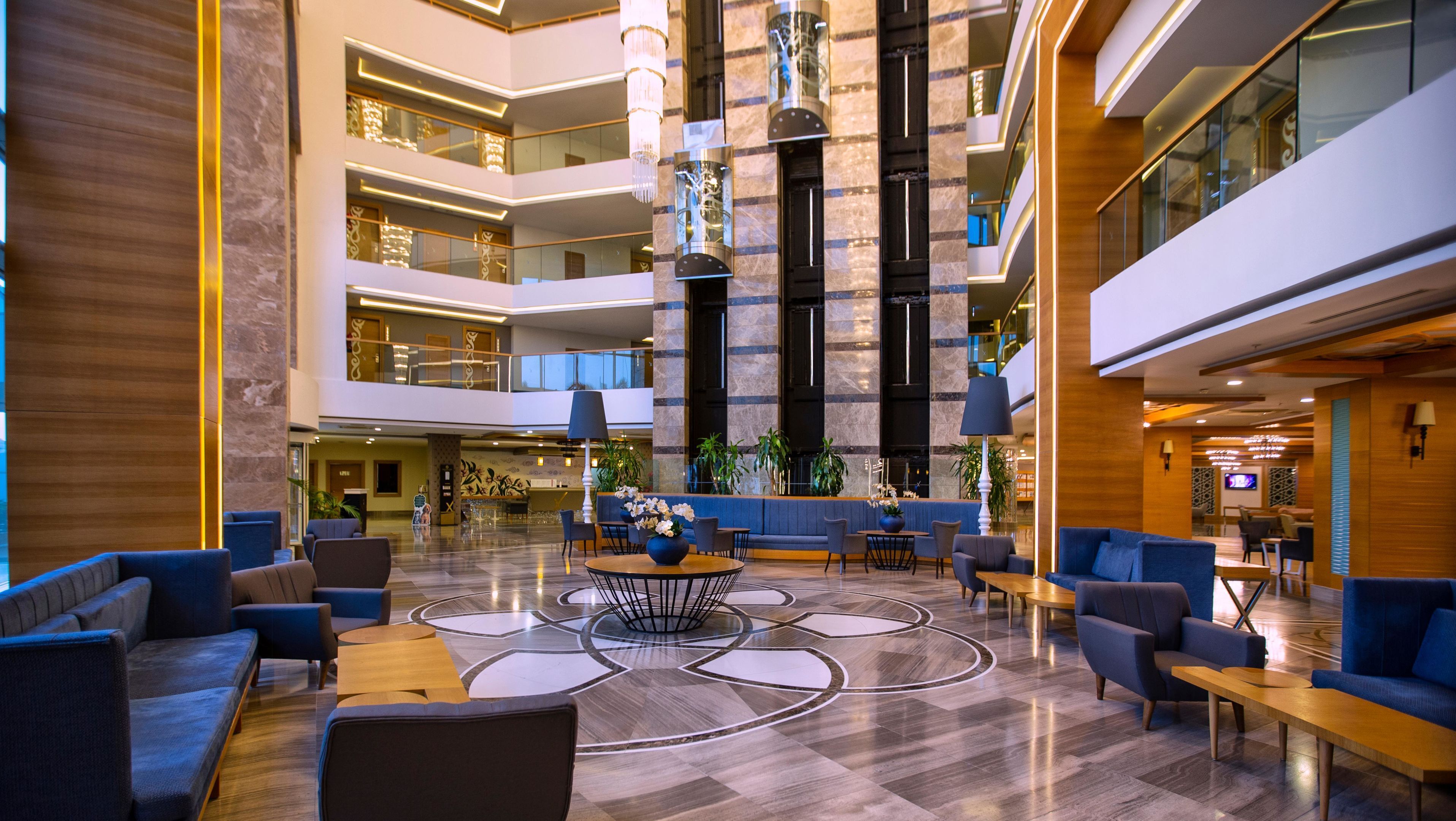Een hotel lobby met meerdere verdiepingen, zitgedeeltes, een receptiebalie en een kroonluchter.