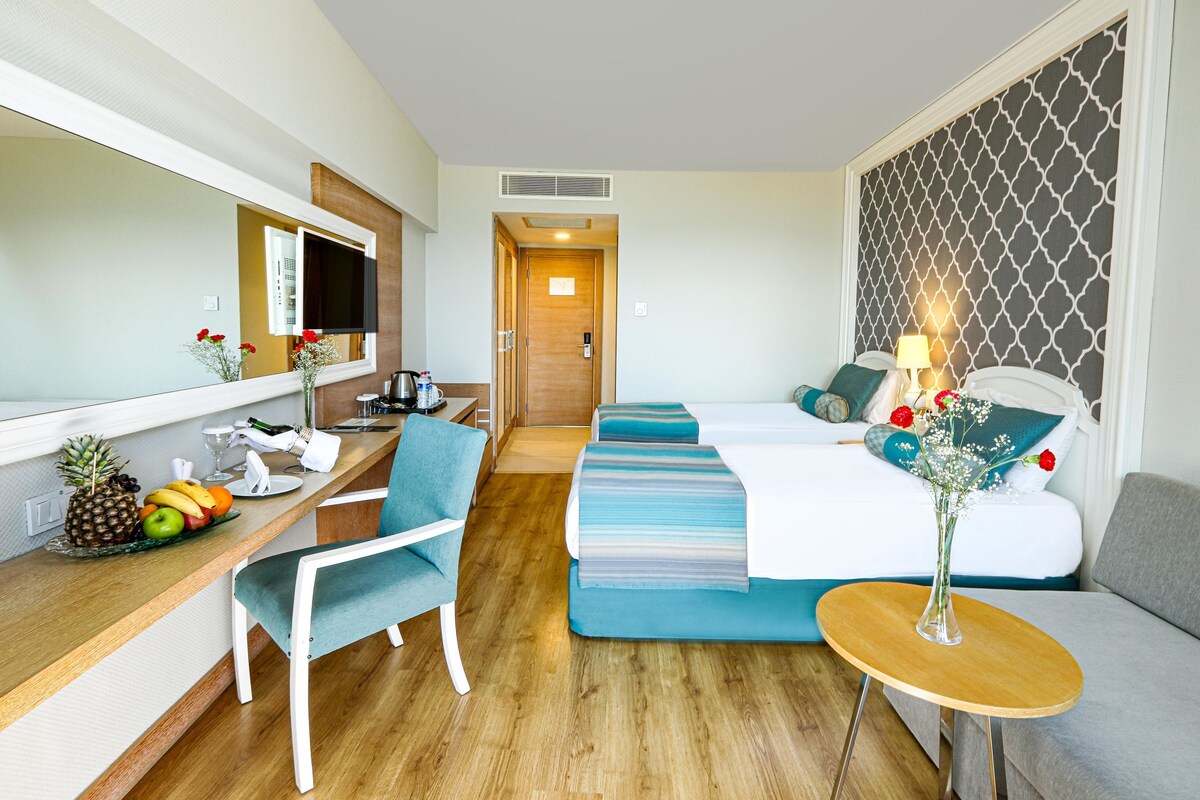 A hotel room with a bed, a desk with a chair, a small table, and a mirror.