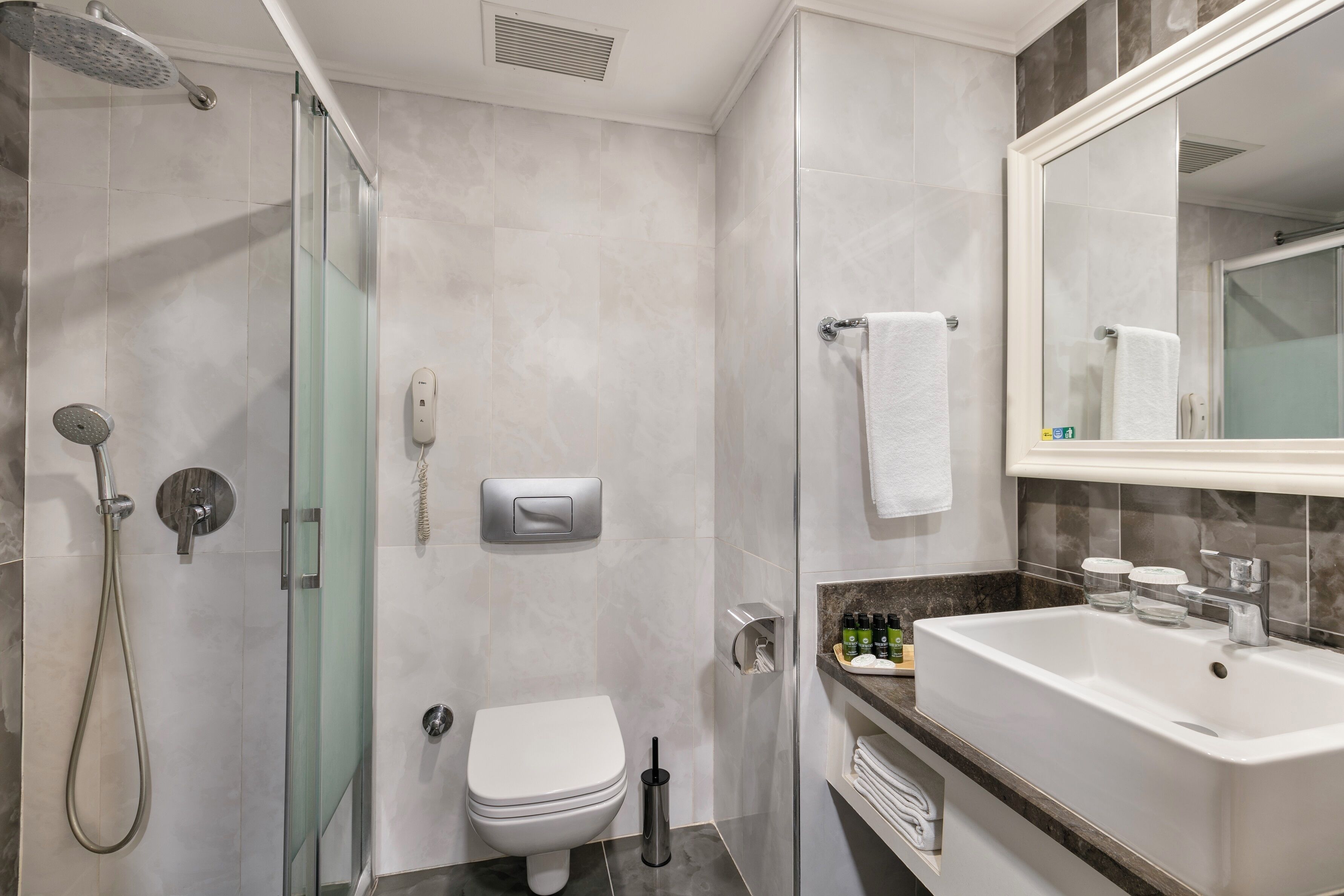 A modern bathroom with a glass-enclosed shower, a white toilet, a sink with a marble countertop, and a large mirror.