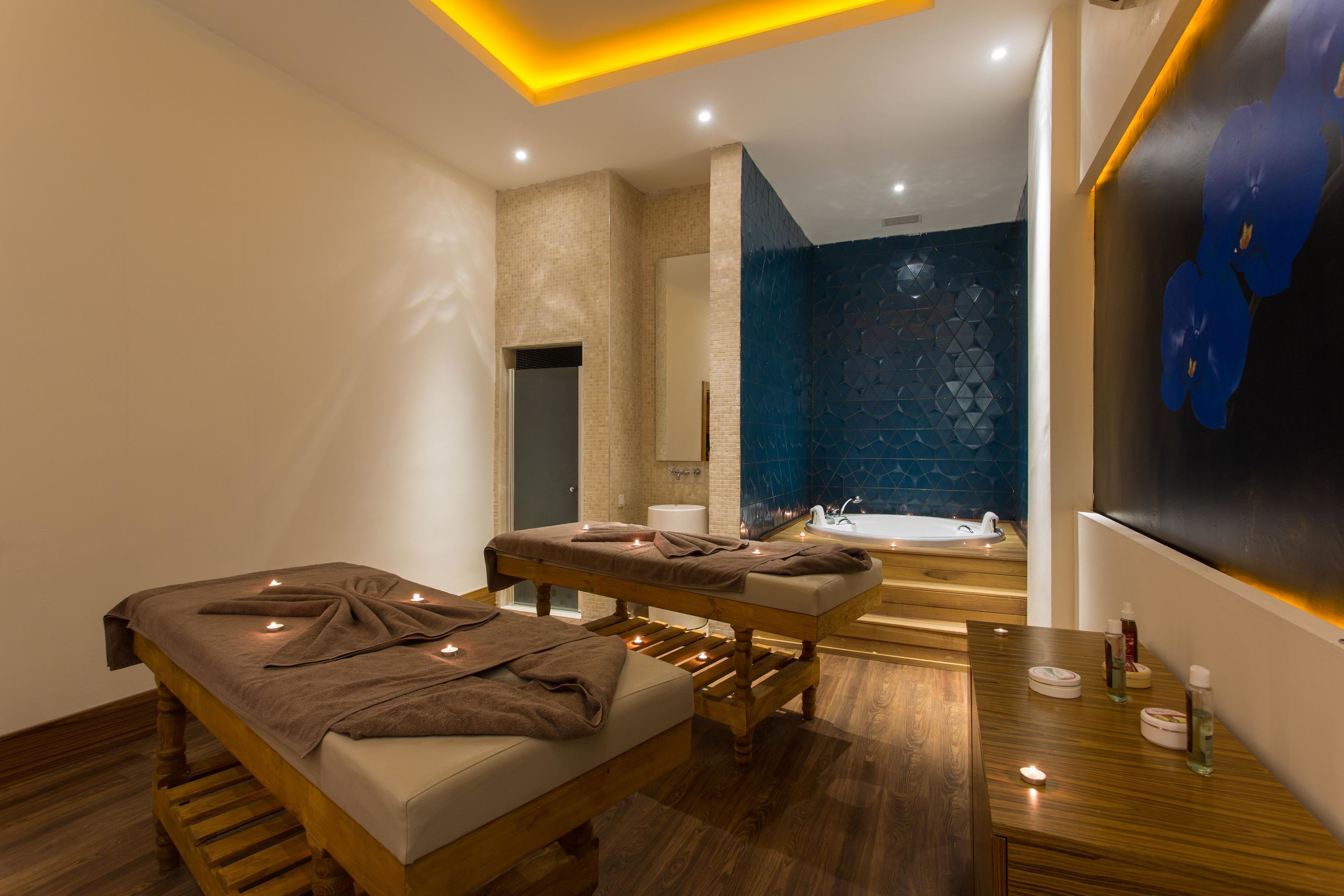 A modern spa room with a wooden massage table, a bathtub, and a blue-tiled wall.