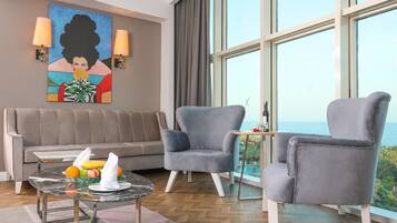 Una habitación moderna con sofá, dos sillones, una mesita con fruta y servilletas, y un ventanal con vistas.