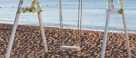 A beach swing set with a sign that reads "#sharewood" and is decorated with greenery.
