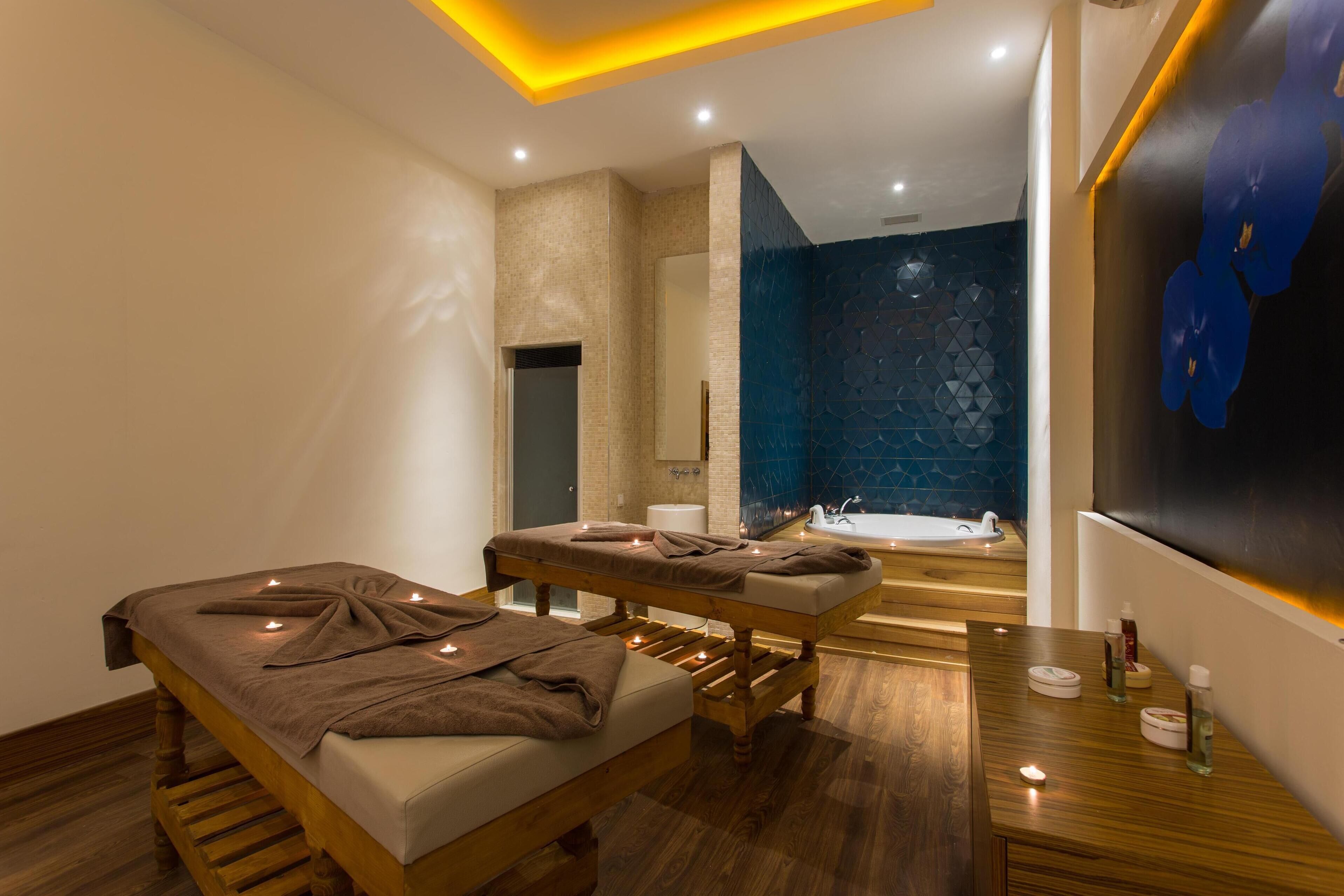 Une salle de spa moderne équipée d’une table de massage, d’un banc en bois, d’un comptoir en bois avec des articles de toilette et d’un mur recouvert de carreaux bleus.