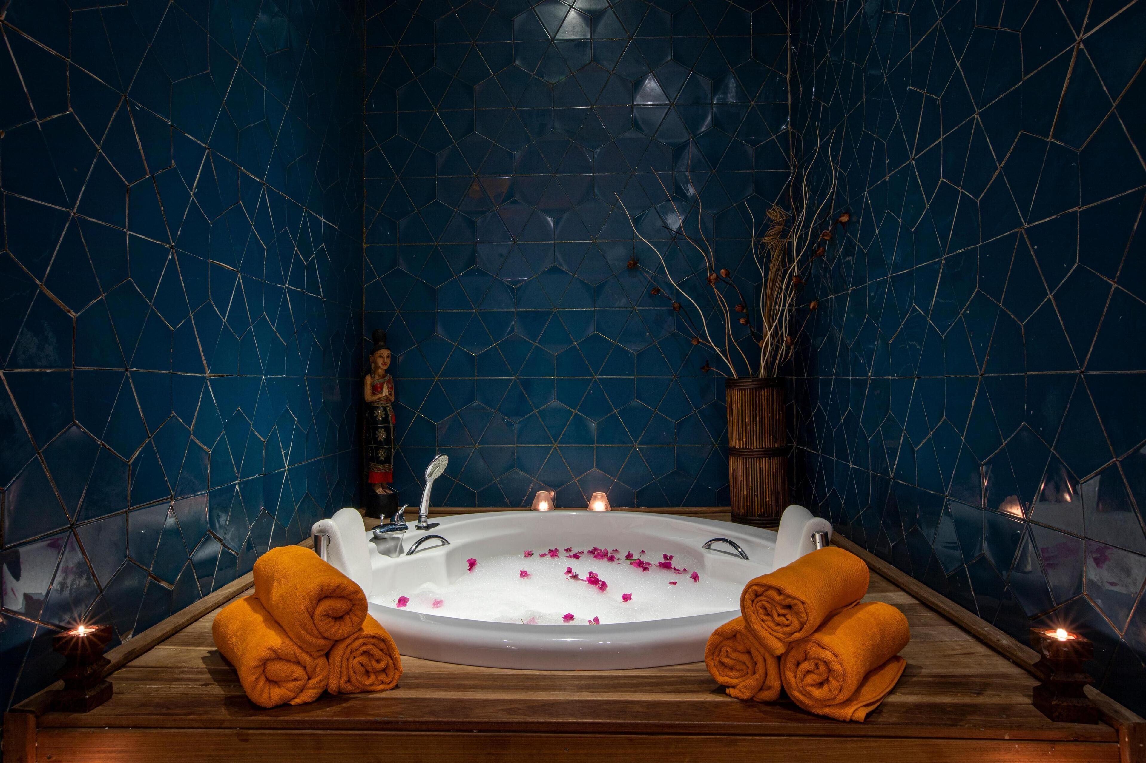 A spa room with a large bathtub, wooden bench, and towels.