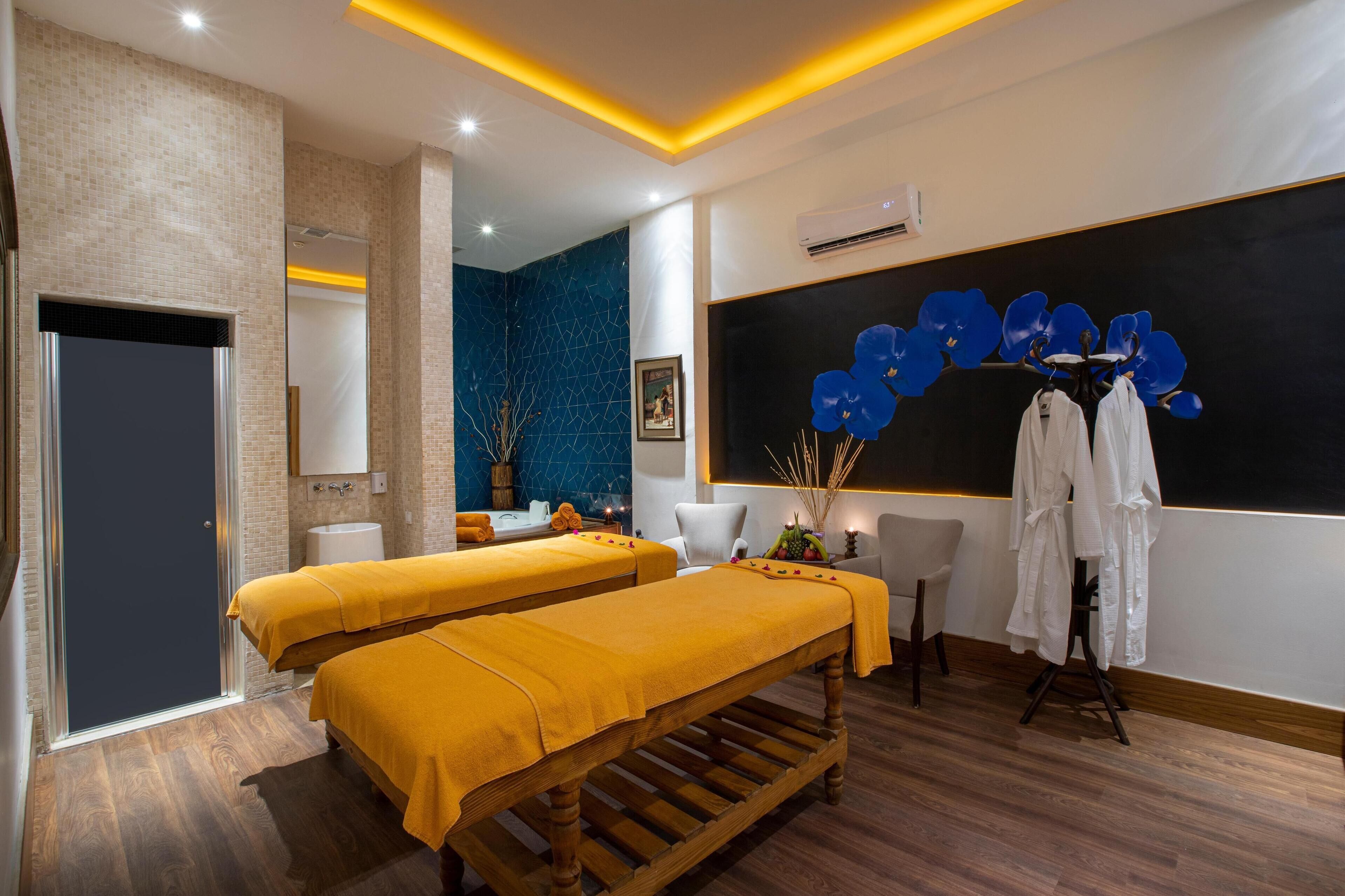 Ein Wellnessraum mit zwei Holzbanken, einem Massagetisch, einer blau gefliesten Wand und einer Tafel mit blauen Blumen.