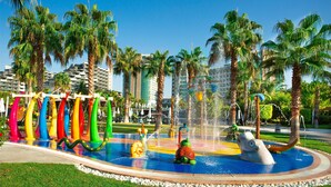 Een waterpark met een kleurrijke glijbaan, een waterattractie in de vorm van een kikker en palmbomen.