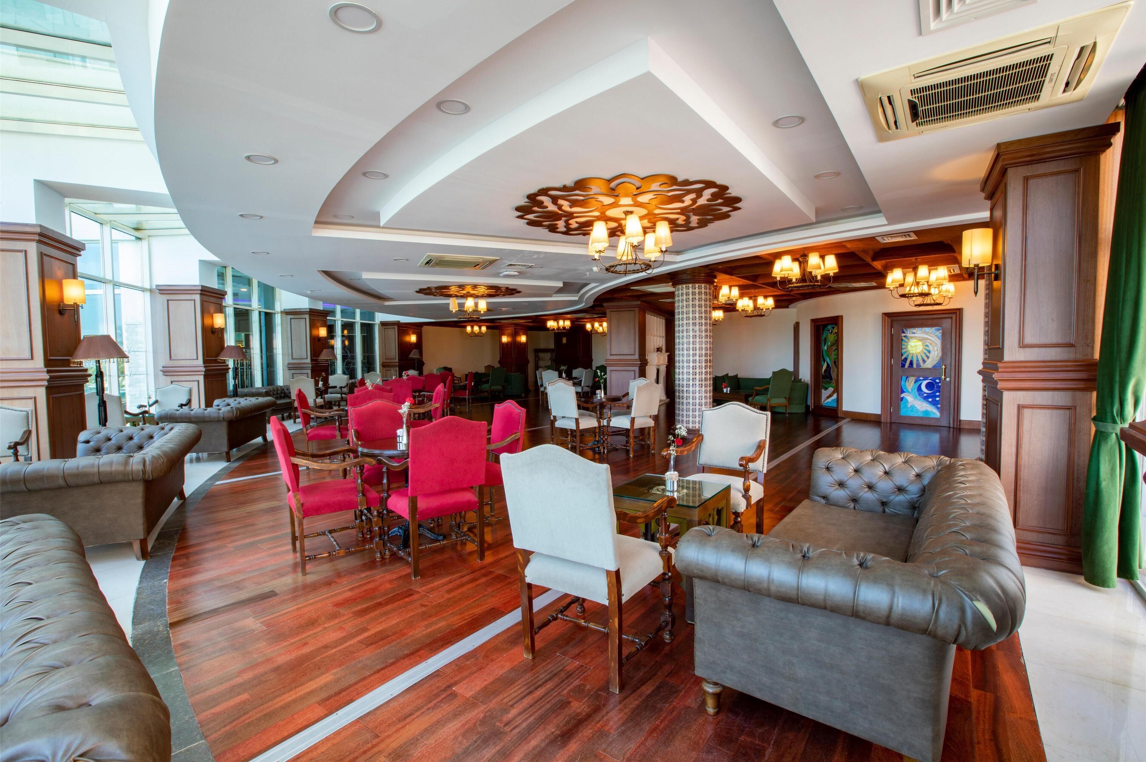 Eine geräumige Lobby mit gewölbter Decke, Ledersofas, roten und weißen Sesseln und einem Kristalllüster.