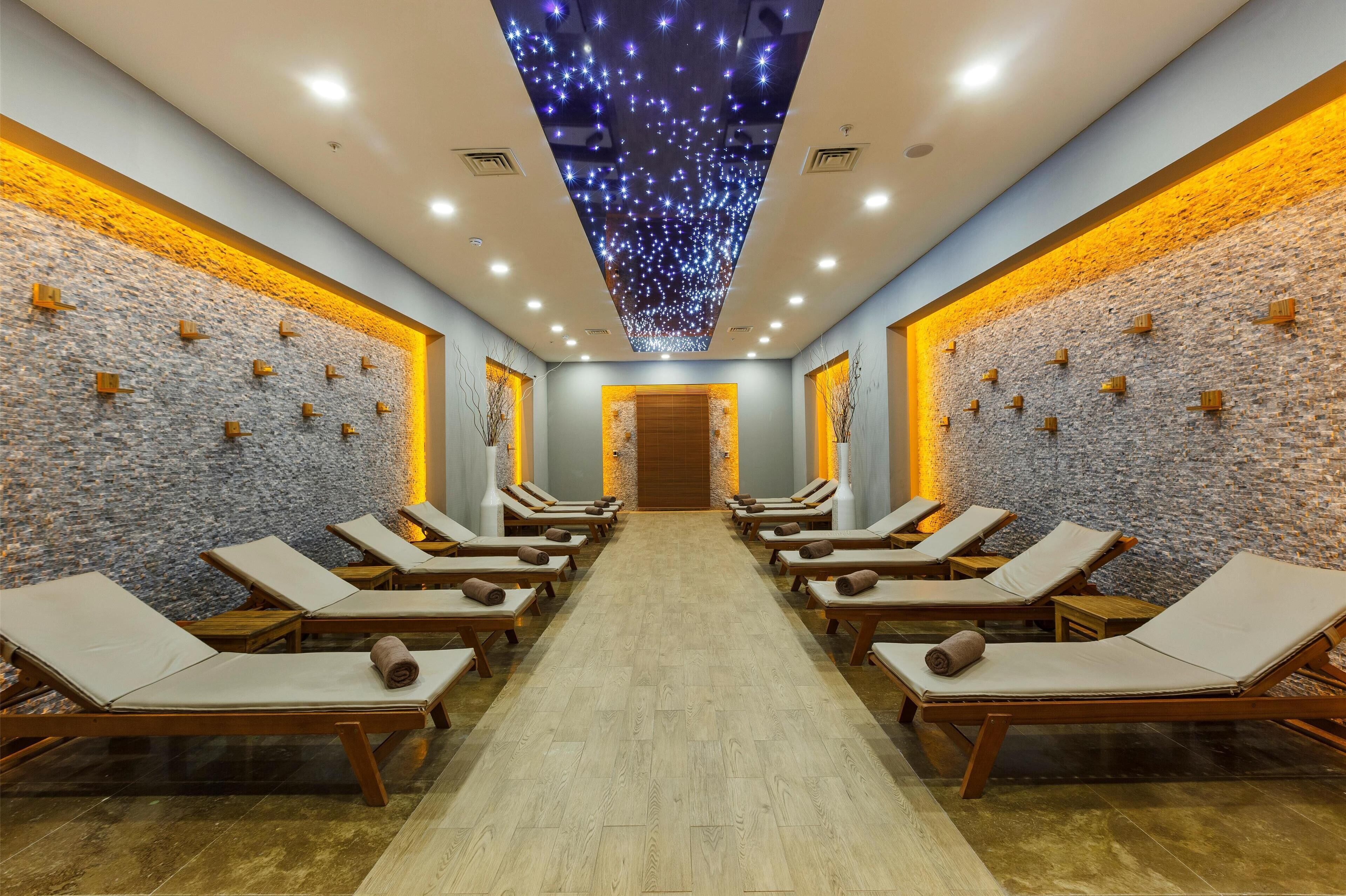 A spa room with wooden loungers, a stone wall, and a ceiling with star-like lights.