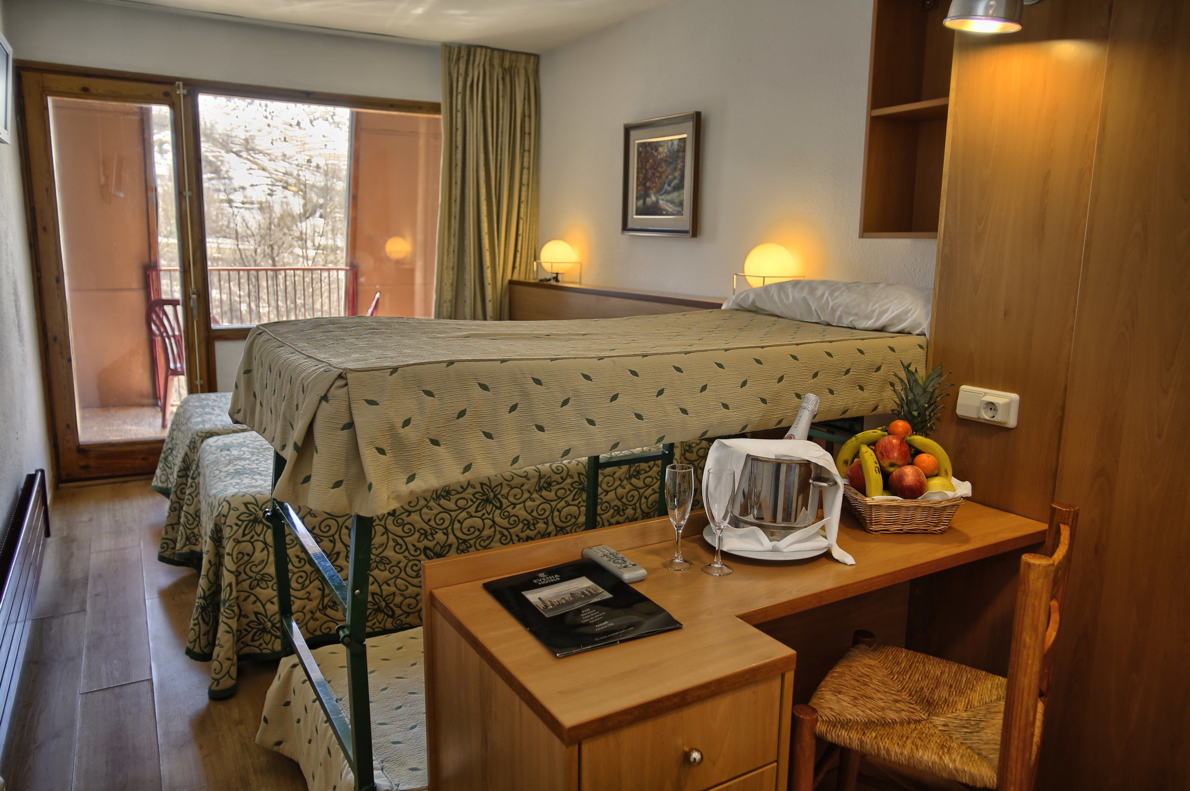A hotel room with a bed, two bedside tables, a desk with a basket of fruit, and a chair.