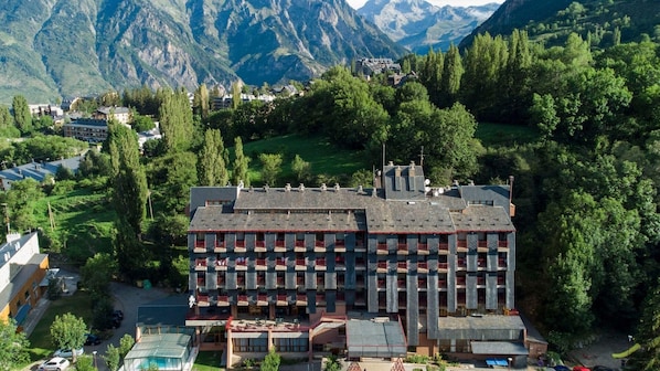 A multi-story hotel with a central courtyard, surrounded by lush greenery and mountains in the background.