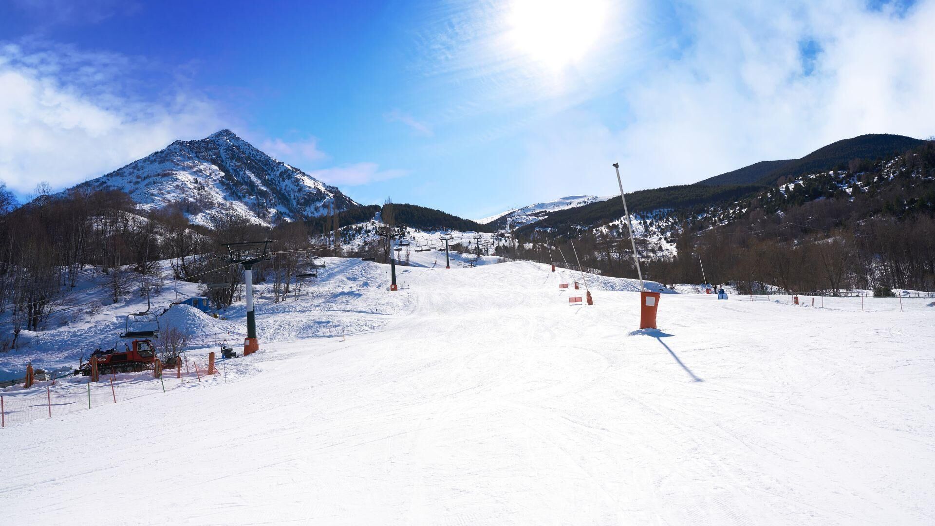 Pista de esquí nevada con remontes, árboles y montañas al fondo.