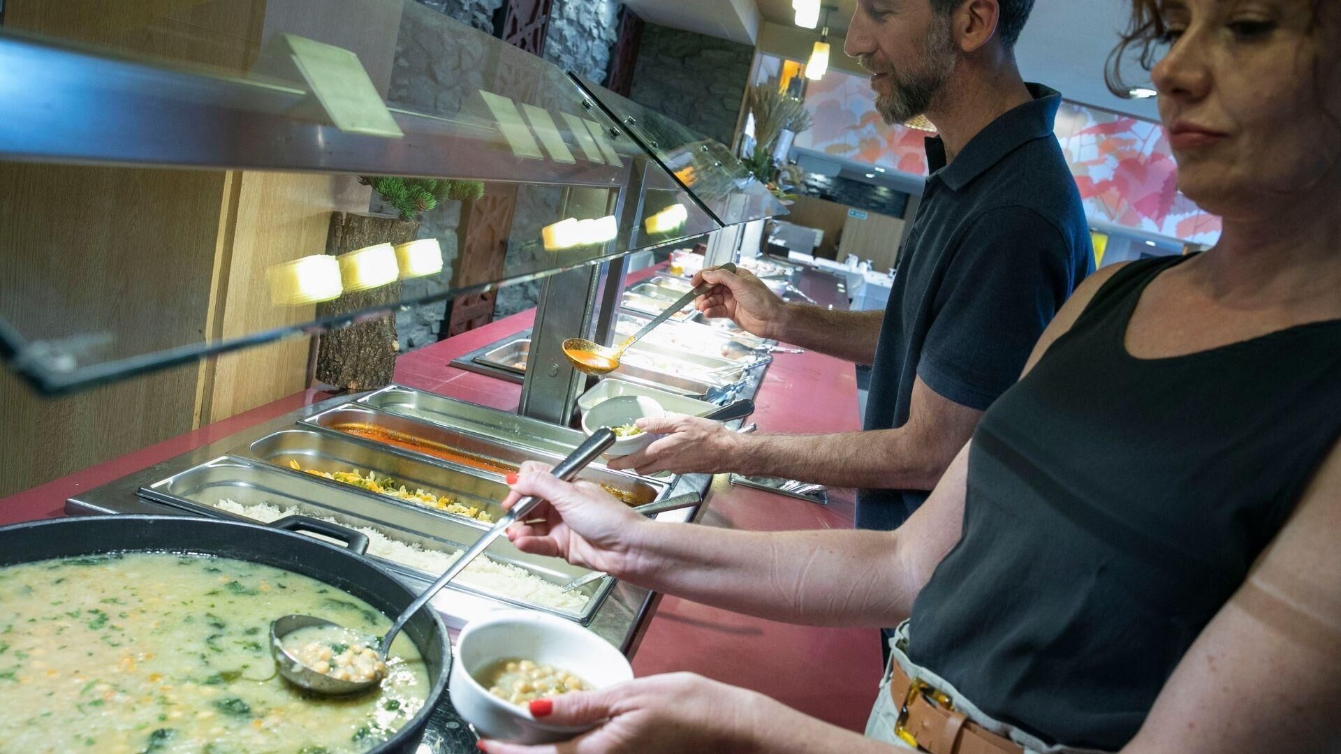 Una mesa de buffet con distintos alimentos y una olla grande de sopa.