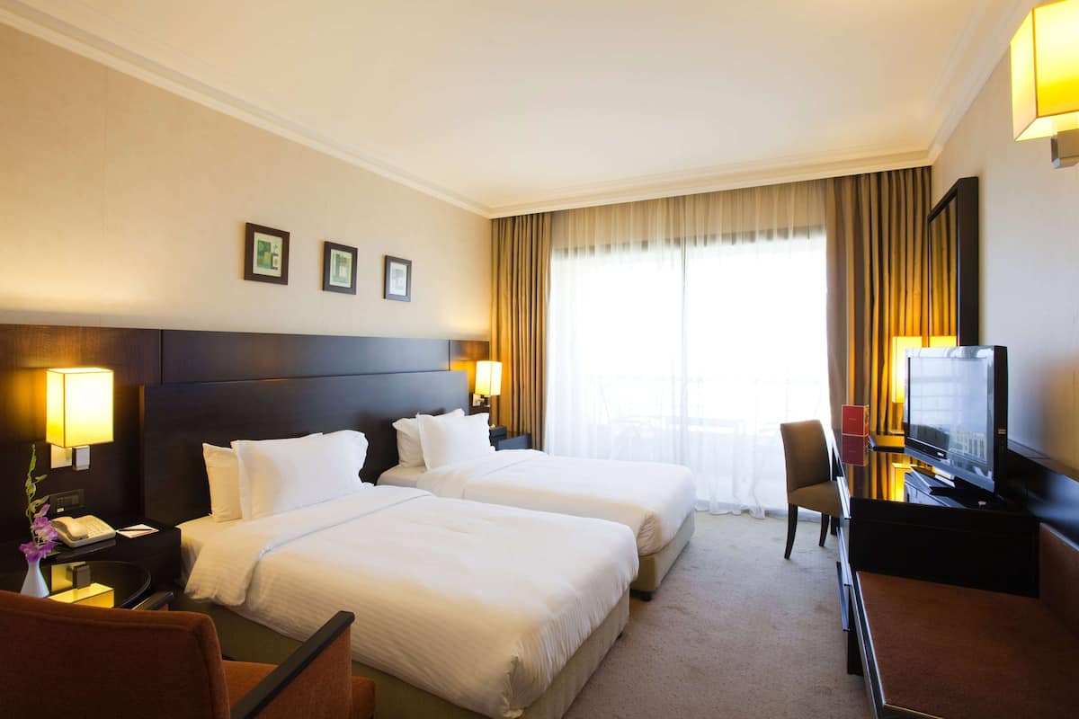 Ein Hotelzimmer mit zwei Betten, einem Schreibtisch mit Lampe, einem Fernseher und einem Sessel.