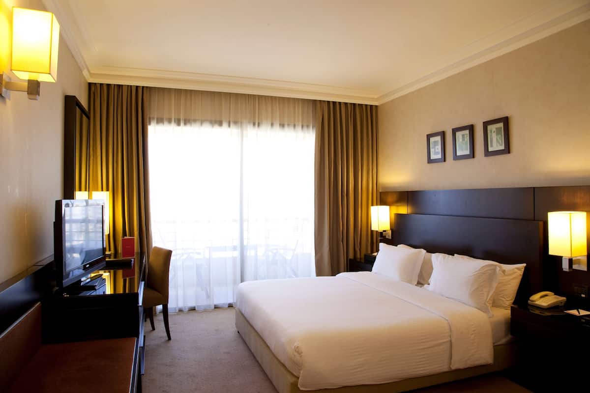 Ein Hotelzimmer mit einem großen Bett, einem Schreibtisch mit Fernseher, einem Sessel und Balkonblick.
