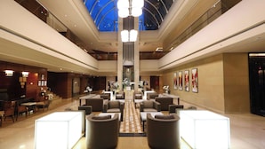 Een ruime lobby met een hoog plafond, een centrale trap en een glazen koepel.