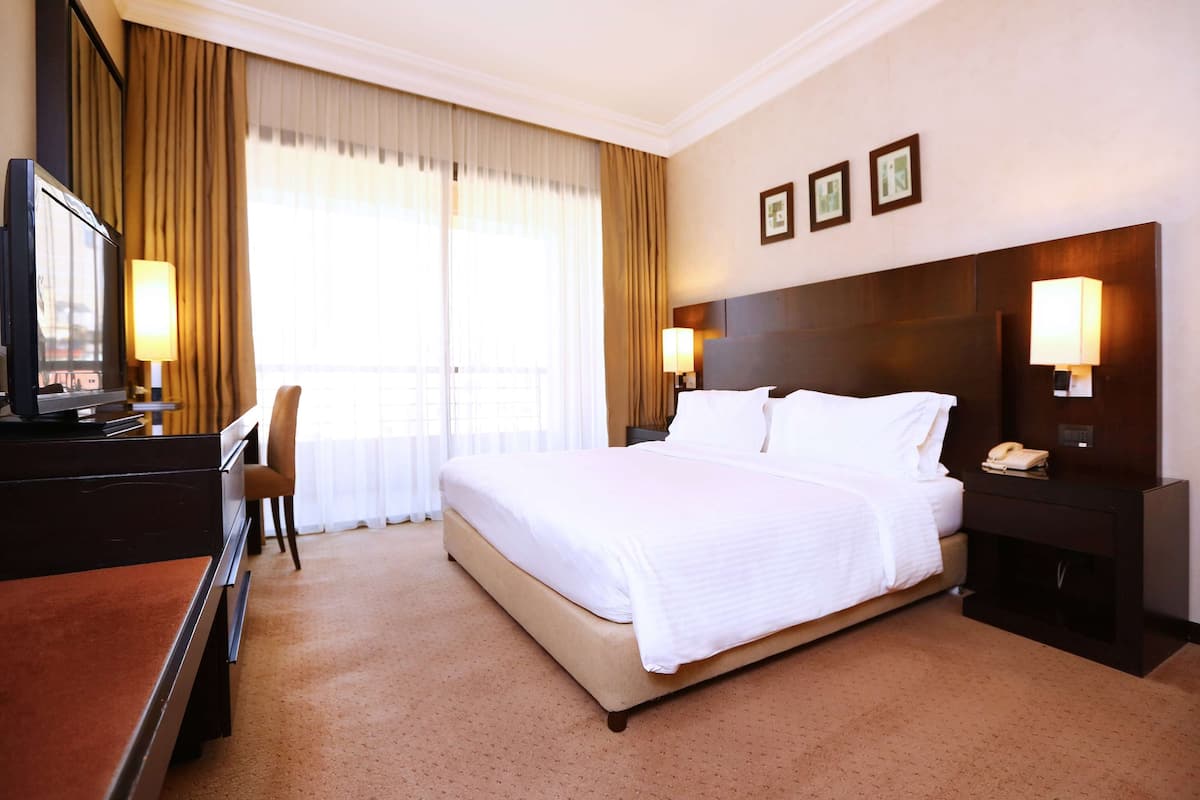 Ein Hotelzimmer mit einem großen Bett, einem Schreibtisch mit Stuhl, einem Fernseher und zwei Nachttischlampen.