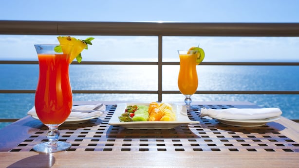 Een tafel met twee drankjes, een fruitschaal en een witte servet, met een prachtig uitzicht op zee.