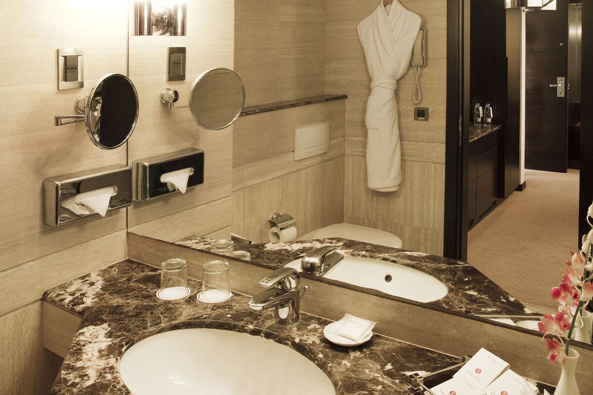 Un baño de hotel con lavamanos de mármol, una bata colgada en la pared y un espejo.