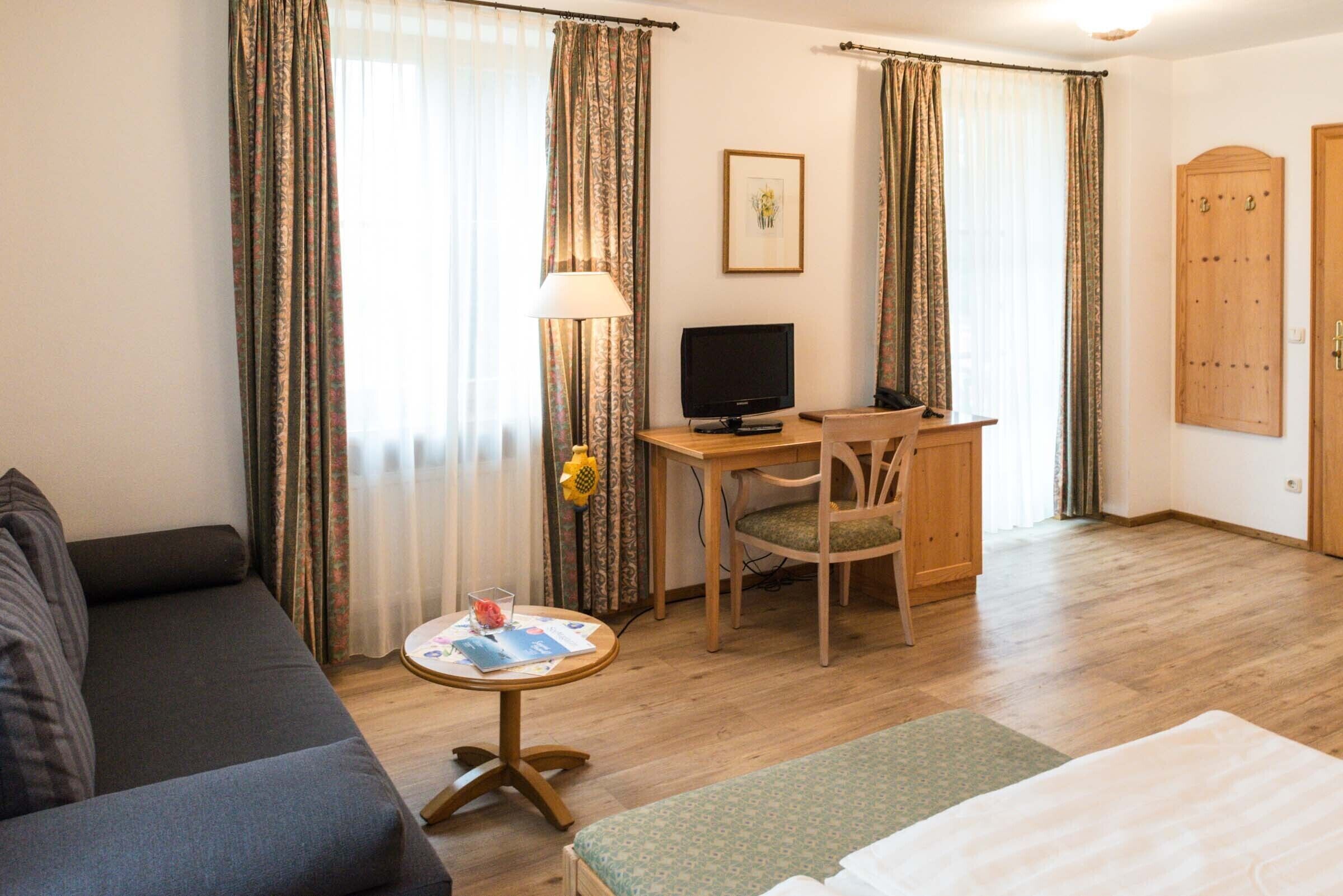 Ein Hotelzimmer mit Sofa, Schreibtisch inklusive Computer, einem kleinen Tisch mit Lampe sowie einem Bett.