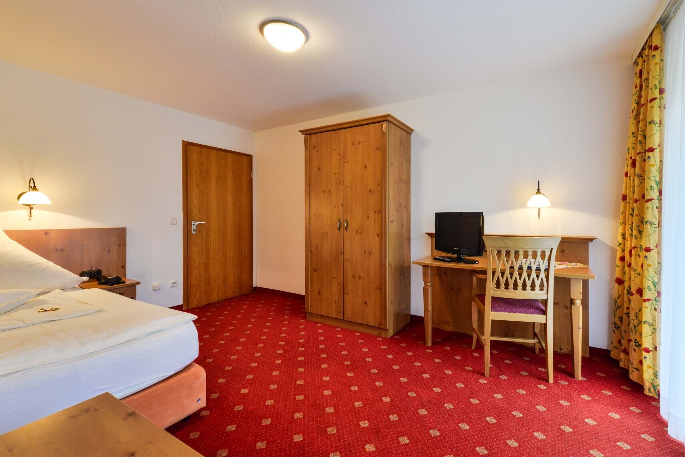 Hotellihuone, jossa on sänky, työpöytä tuolilla, televisio ja vaatekaappi.