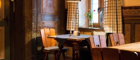 Un área de comedor con una mesa y sillas de madera, una lámpara colgante y un ventanal con cortinas.