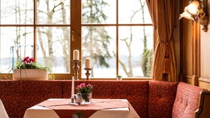 Een gezellig zitgedeelte met een tafel, beklede bankjes en een groot raam met uitzicht op bomen.