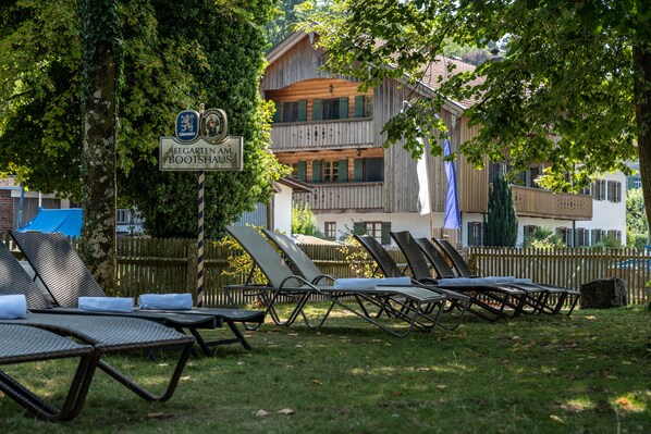 A row of sun loungers in a grassy area with a wooden building in the background.