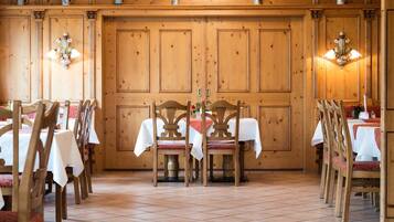 Un comedor con paneles de madera, manteles blancos y sillas con cojines rojos.