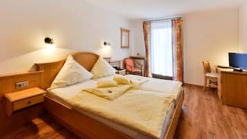Een hotelkamer met een houten bed, nachtkastjes, een bureau met stoel, een televisie en een raam met gordijnen.