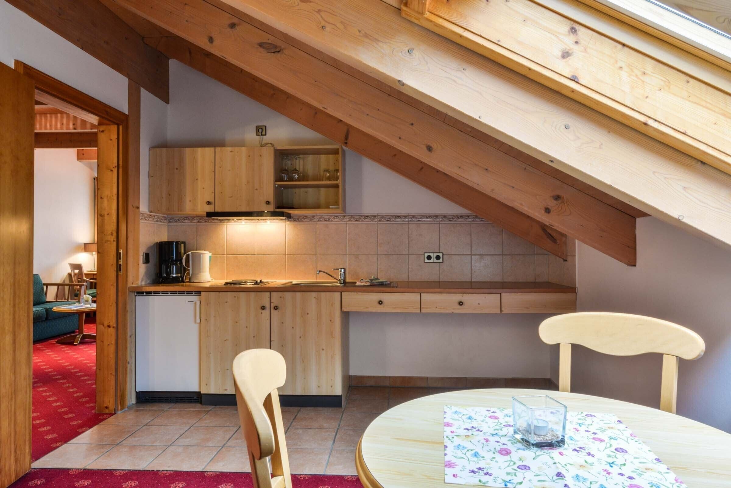 A kitchen with wooden cabinets, a dining table with chairs, and a red carpeted area.