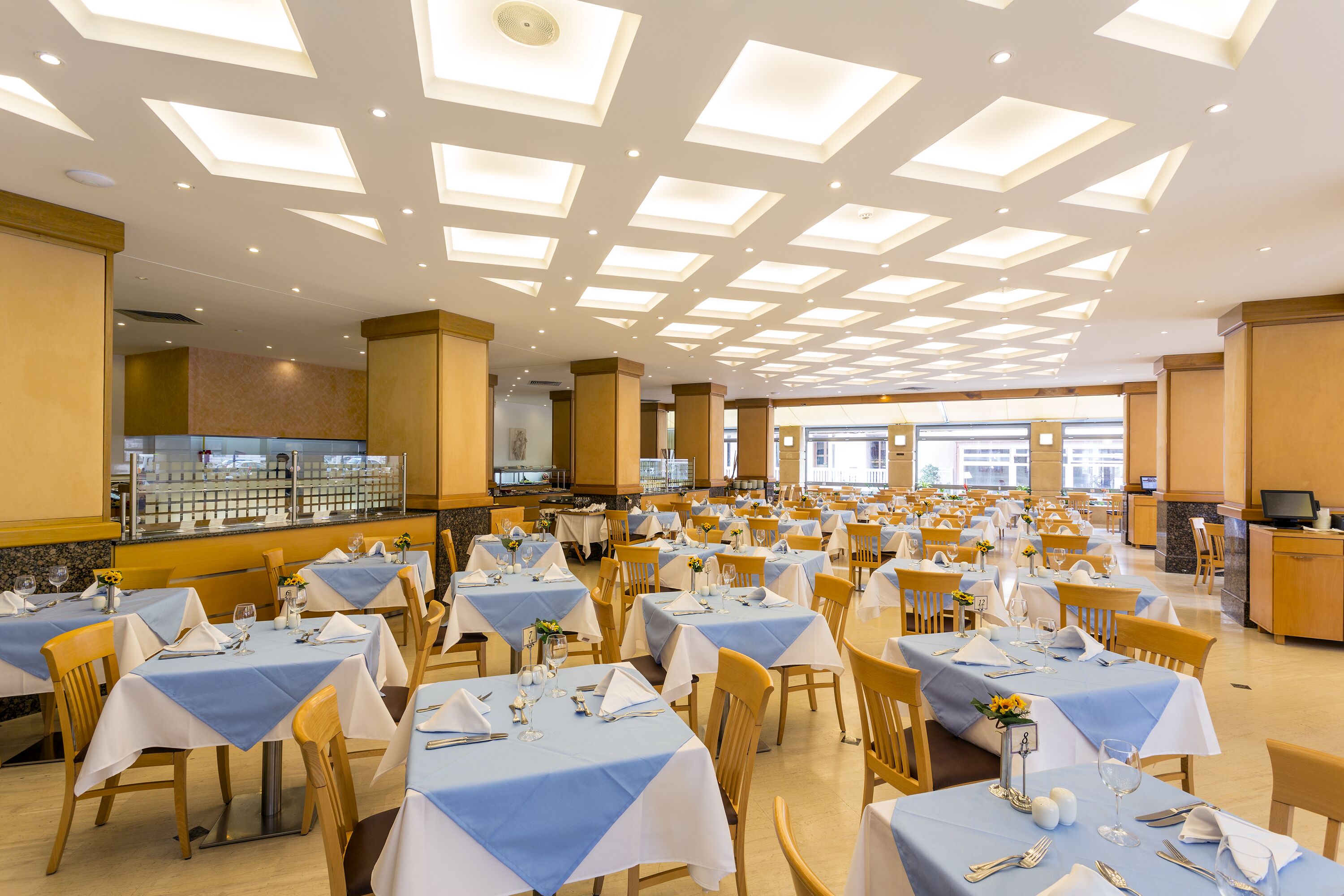 A large dining area with multiple tables set for guests, featuring a modern ceiling design with recessed lighting.