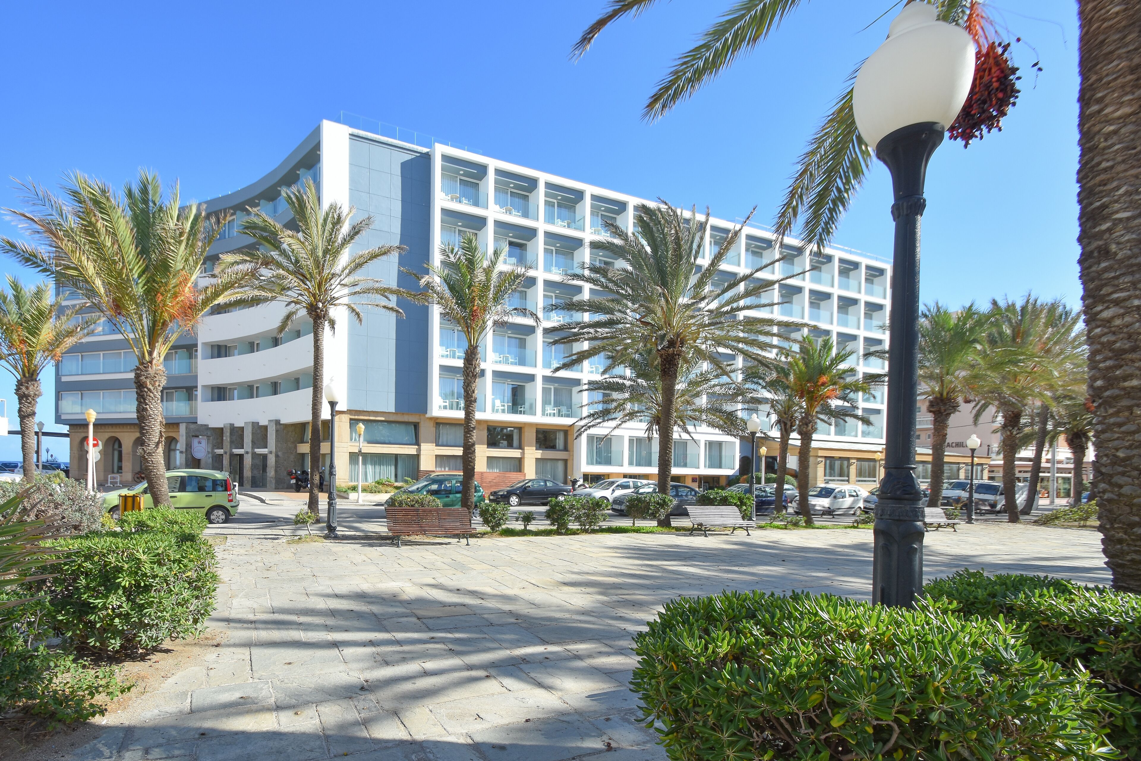 A modern hotel with a curved facade, palm trees, and a paved walkway.