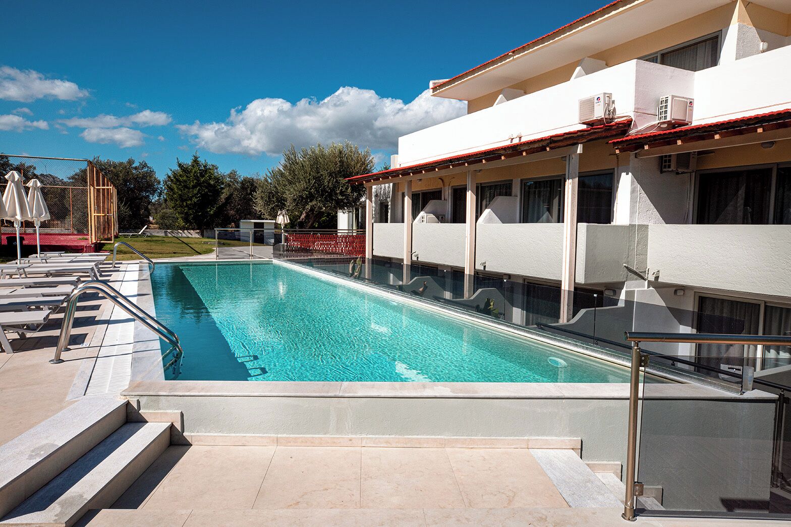A swimming pool with steps leading into it, surrounded by a building with large windows and a red roof.