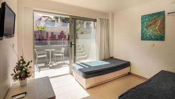 Ein kleiner, moderner Raum mit Bett, Fernseher, Tisch mit Stühlen und Blick auf einen Balkon mit Gartenmöbeln.