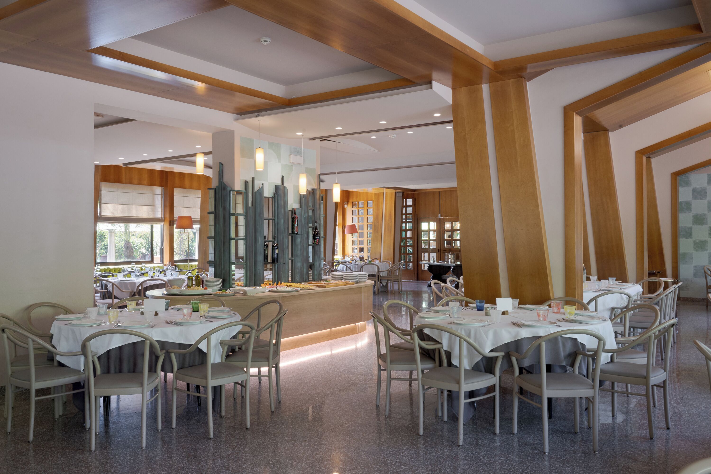 A modern dining area with multiple tables and chairs, a central counter, and large windows allowing natural light.