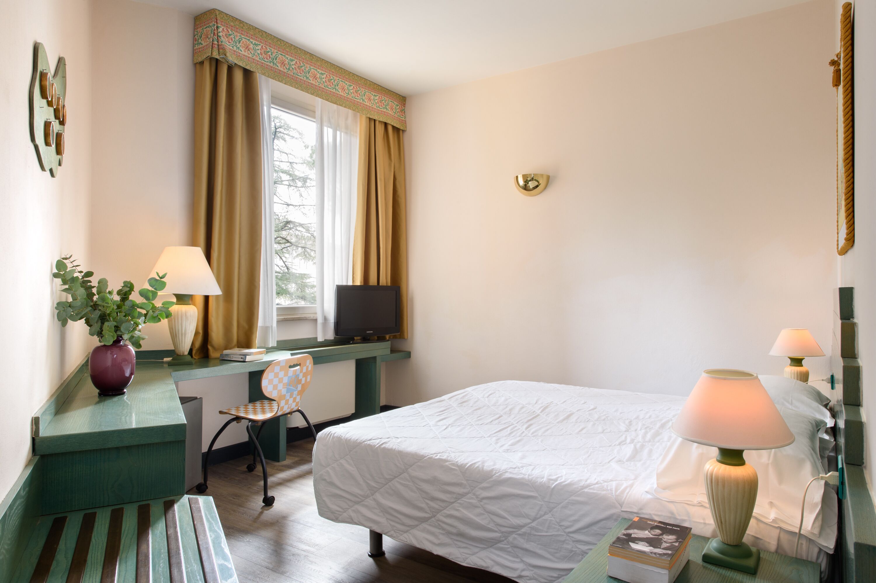 A hotel room with a bed, desk, chair, television, and two lamps.