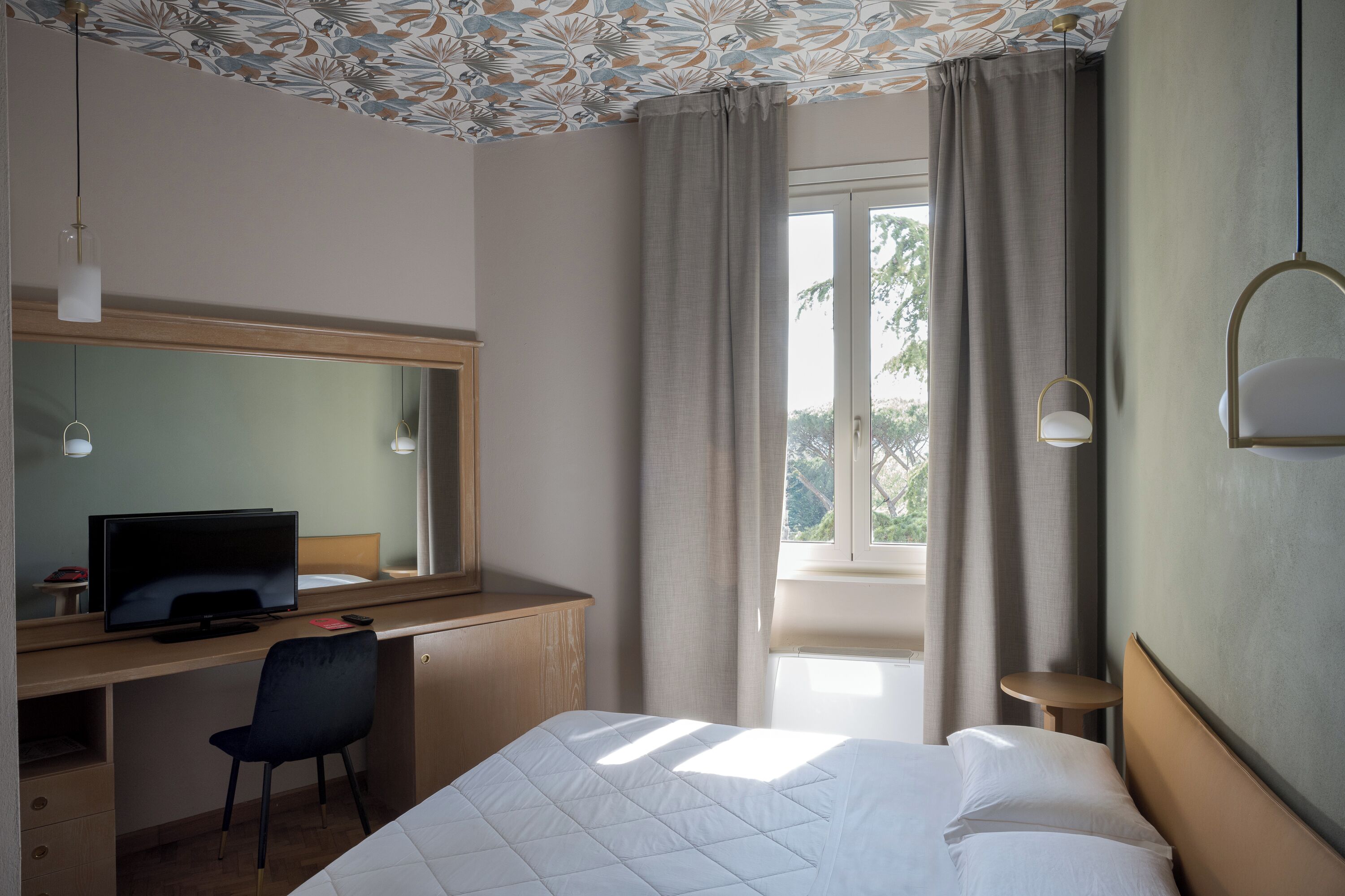 Camera d'albergo con letto, scrivania, sedia e un'ampia finestra con tende.