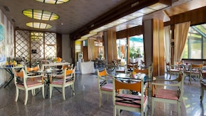 A spacious restaurant with high ceilings, wooden beams, and large windows allowing natural light. Tables and chairs are arranged for dining. - Grand Hotel Panoramic (Montecatini Terme)
