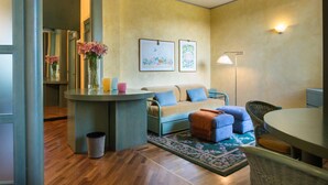 A cozy living room with a sofa, ottoman, and a round table with chairs. There are framed pictures on the wall and a vase with flowers on the table. - Grand Hotel Panoramic (Montecatini Terme)