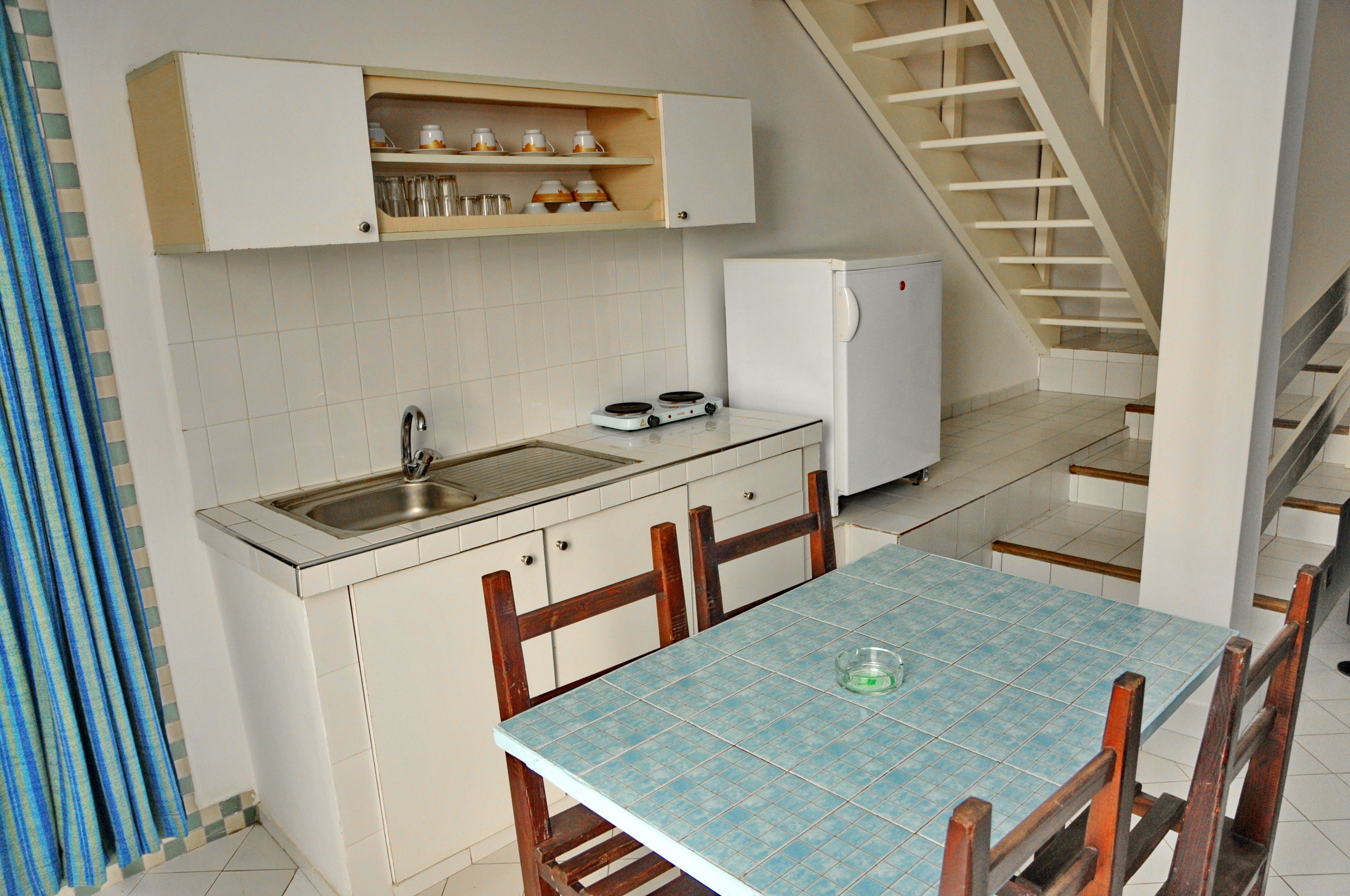 Una cocina compacta con pileta, estufa y heladera pequeña. Cuenta con una mesa de comedor con sillas y una escalera que sube a otro nivel.