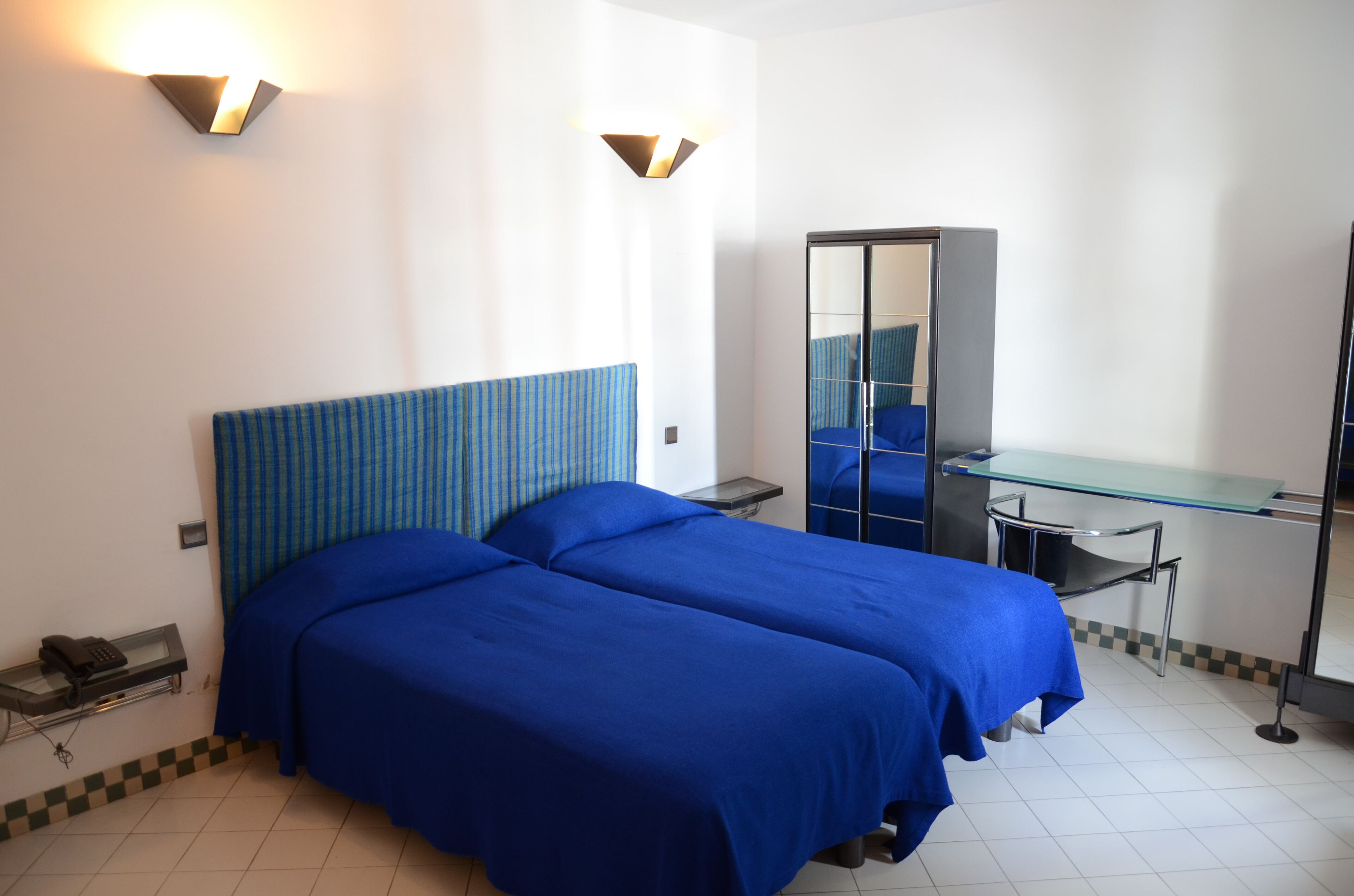 A hotel room with two beds, a desk, a chair, a mirror, and a telephone.