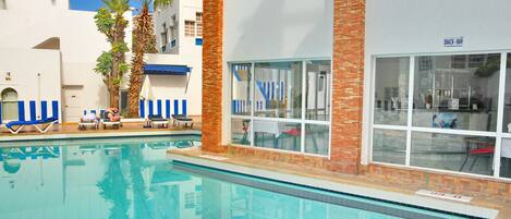 Una piscina con sillones de descanso y un bar de aperitivos.