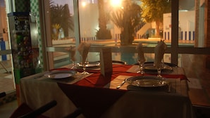 A dining table set with plates, cutlery, and glasses, with a view of palm trees and a building through the window. - Tagadirt Appart-Hotel (Agadir)