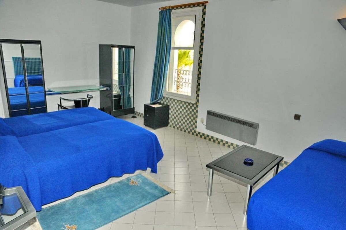 A room with two beds, a desk, a chair, a mirror, a window with curtains, and a radiator.