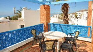 A terrace with a white table and four chairs, blue decorative railings, and a view of buildings and palm trees. - Tagadirt Appart-Hotel (Agadir)