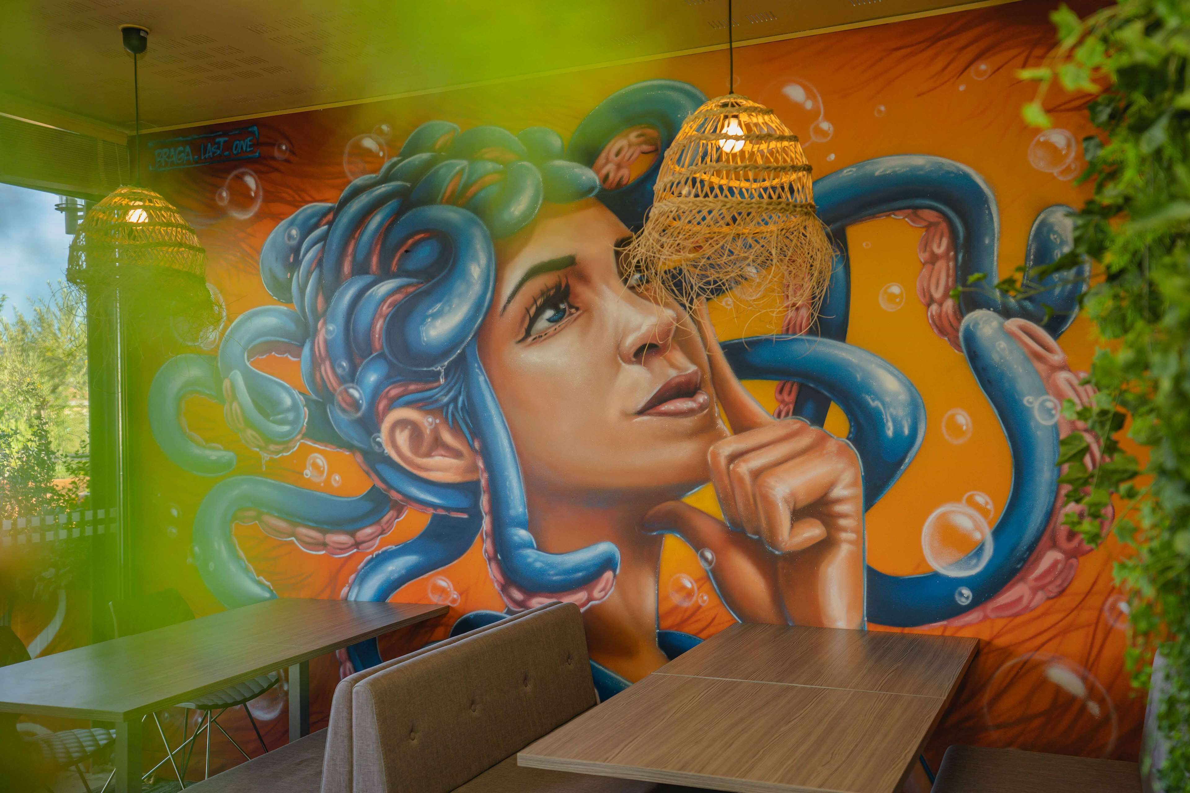 L’intérieur d’un restaurant, avec une fresque représentant une femme et un poulpe, un luminaire suspendu et une vue sur l’extérieur.
