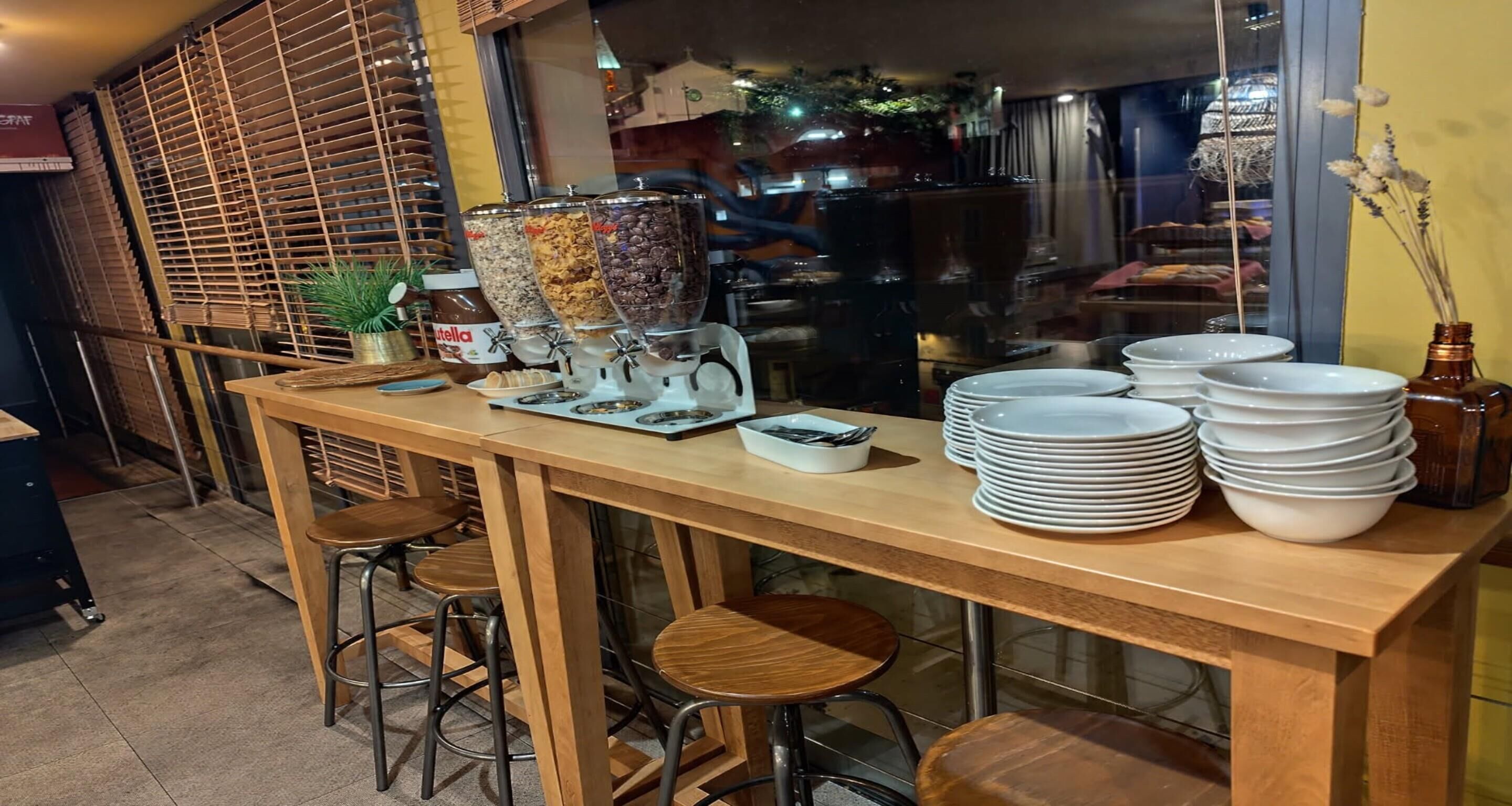 A bar area with a wooden counter, stools, a coffee machine, and a condiment dispenser.