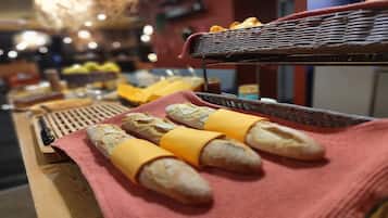 A wooden table with baguettes wrapped in yellow cheese, a wicker basket, and a red cloth.