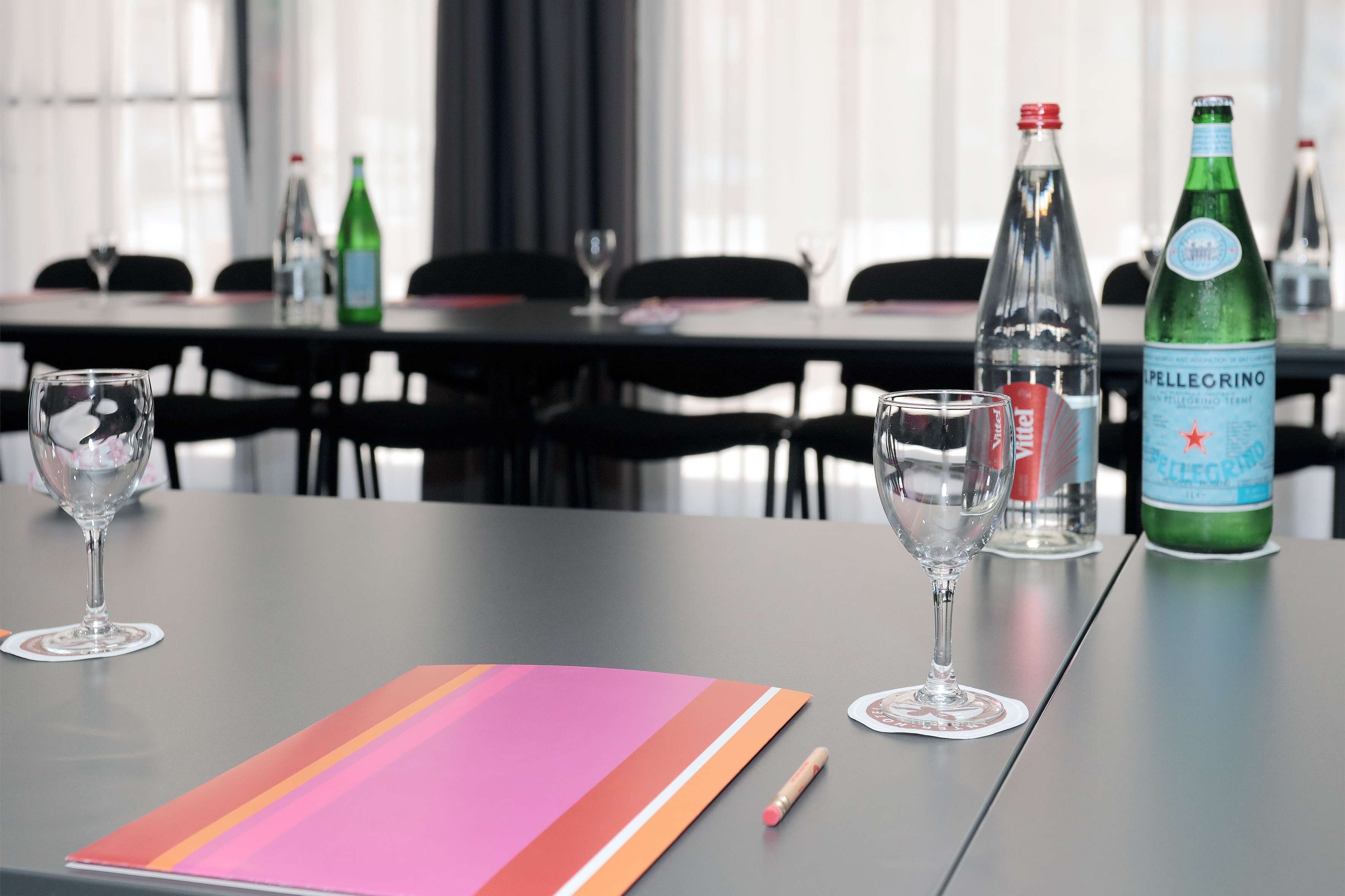 A table with two glasses, a colorful folder, a pen, and two bottles of Pellegrino water.